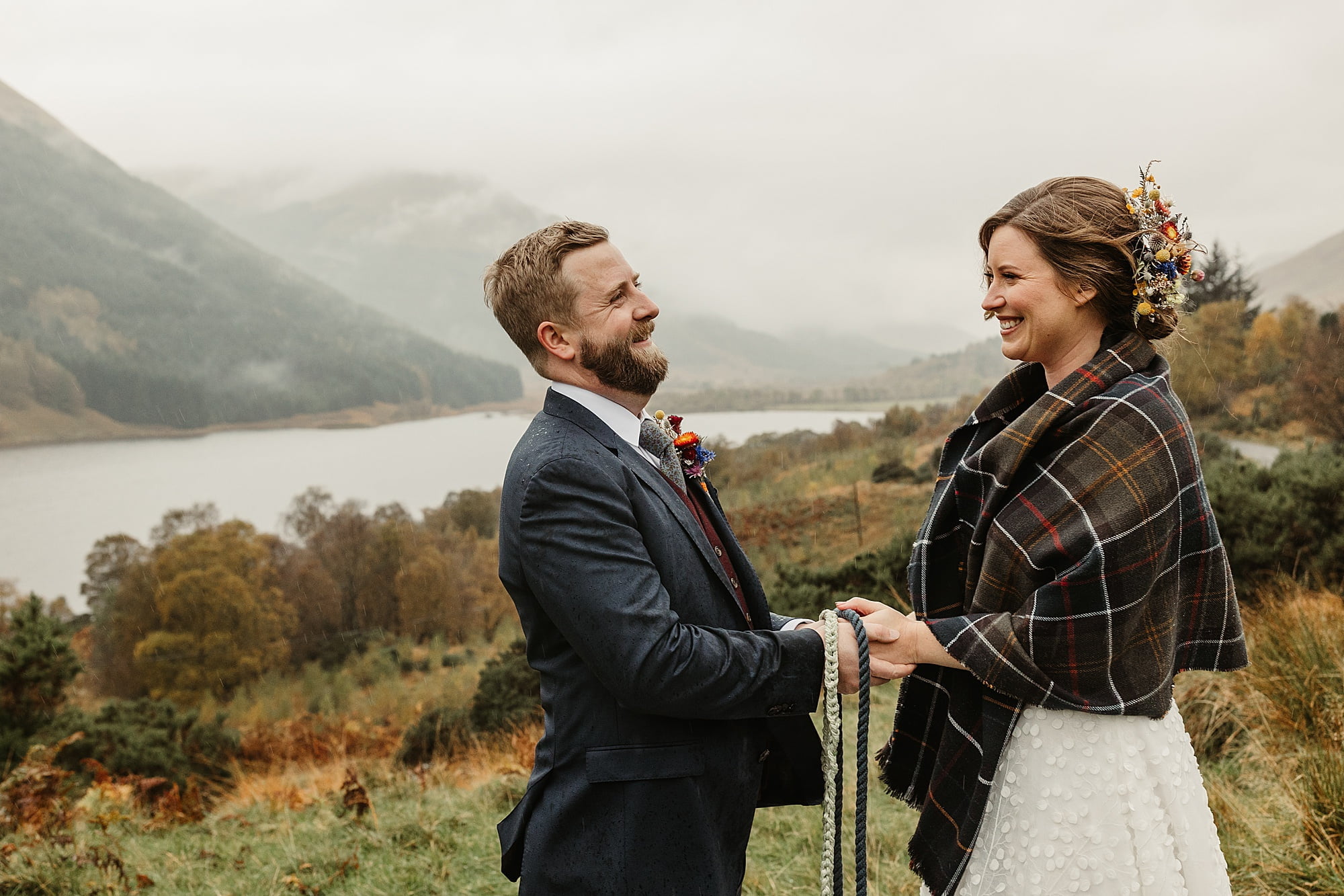 monachyle mhor ceremony outside elopement in the rain with umbrella bride and groom tartan blanket hand fastening