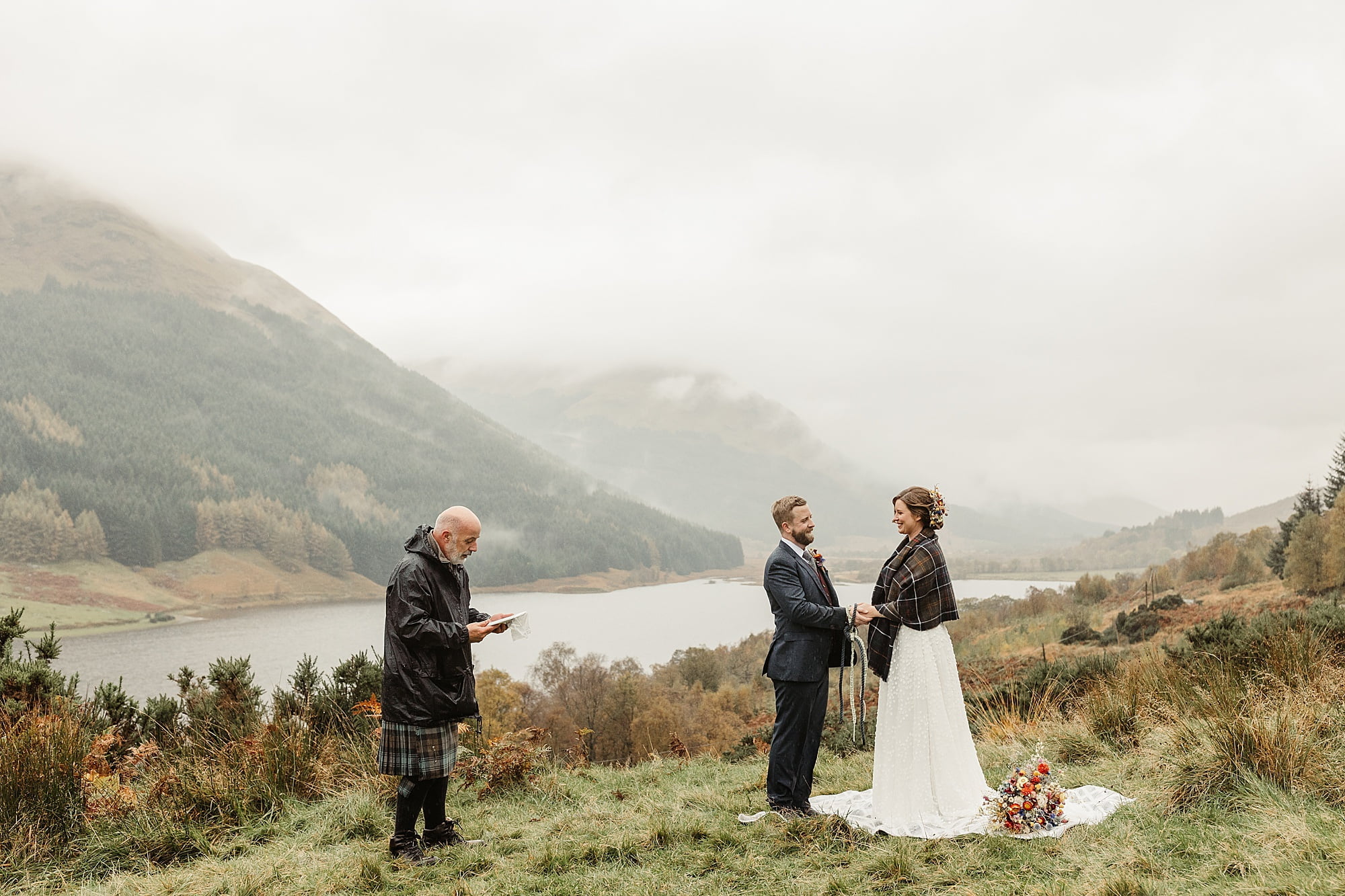 monachyle mhor ceremony outside elopement in the rain with umbrella bride and groom tartan blanket hand fastening gary the humanist