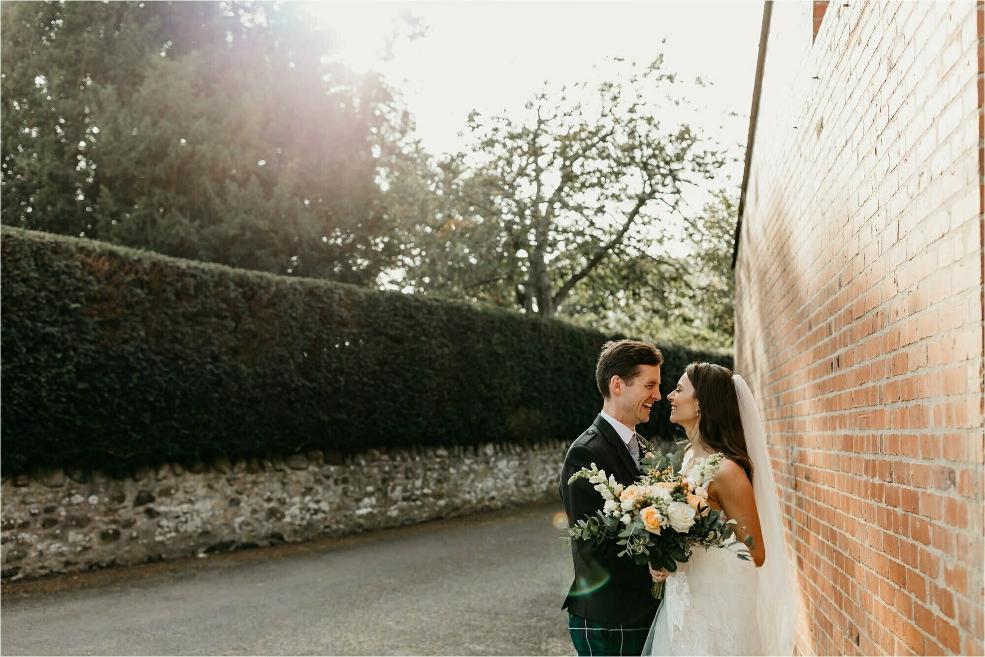 farm micro wedding scottish borders bride groom against red brick wall with sun flare