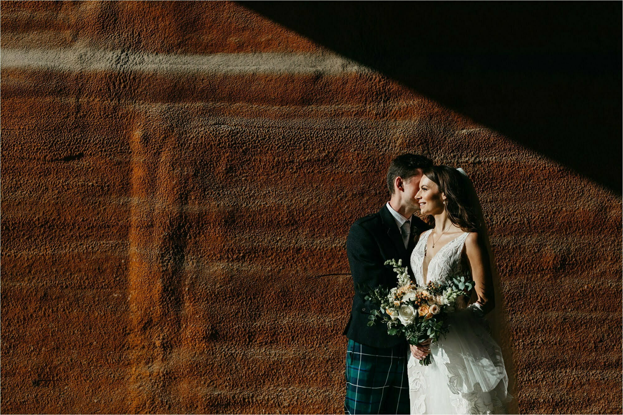 farm micro wedding scottish borders bride groom against red wall with shadows